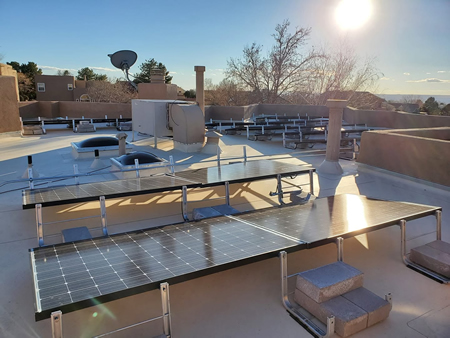 Technician rinsing rooftop solar with deionized water under bright New Mexico sun